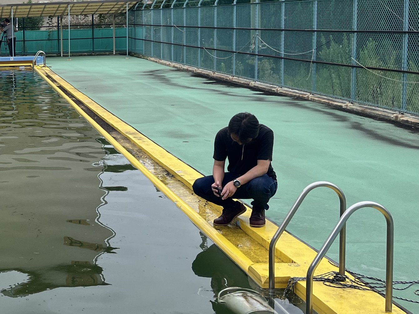 プールサイドにしゃがんで水を採取する様子